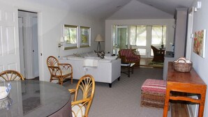 A cozy living room with a white sofa, two wicker chairs, a dining table, and a kitchen area with a white countertop and a lamp. - Best Value in Seabrook - Heron Run (Seabrook Island)