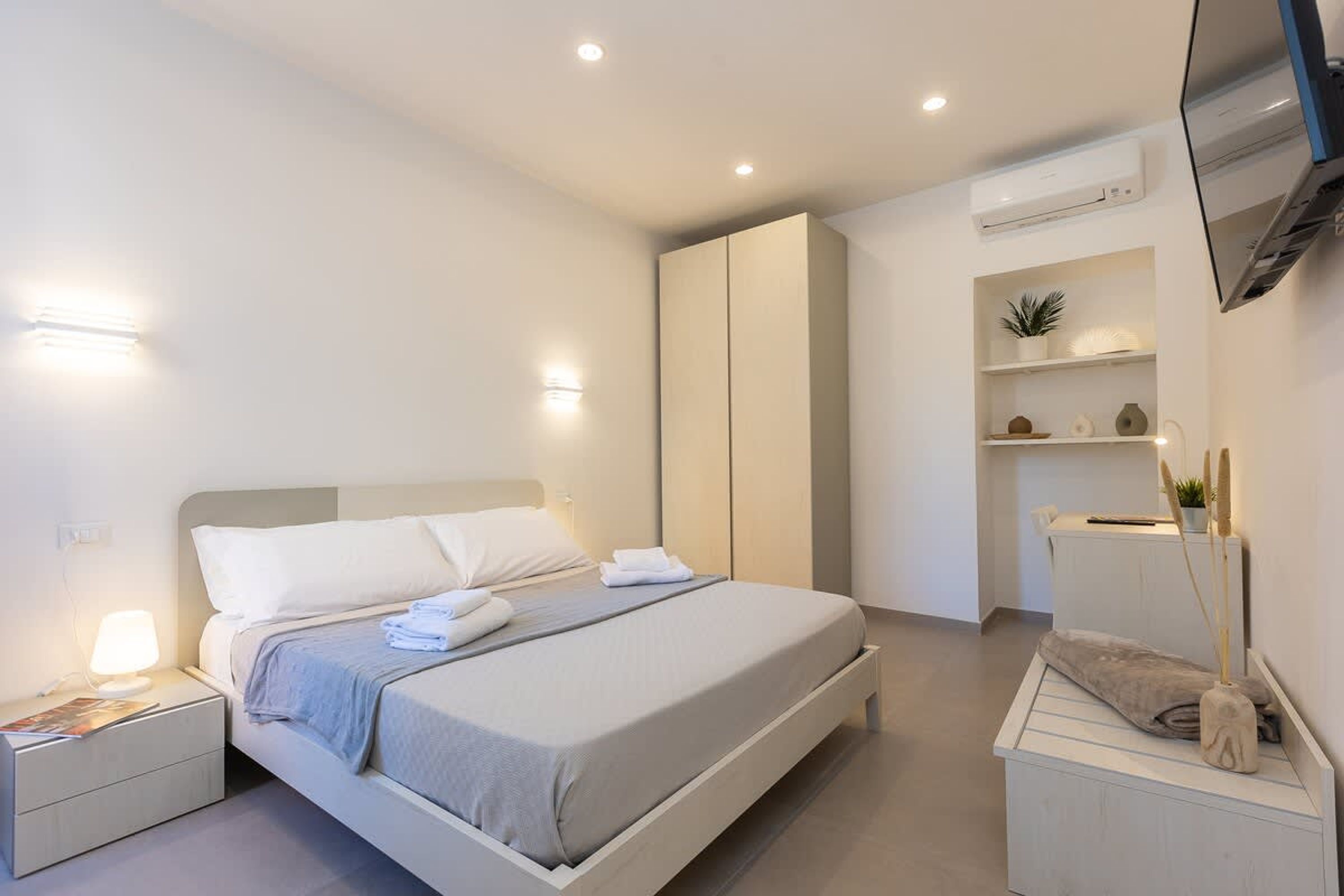 A modern bedroom with a bed, bedside tables, a wardrobe, and a TV mounted on the wall.