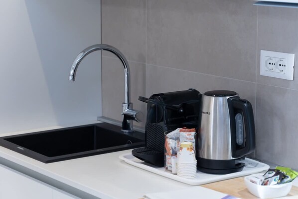 Une cuisine moderne avec un évier noir, une machine à café et une bouilloire posés sur le plan de travail.