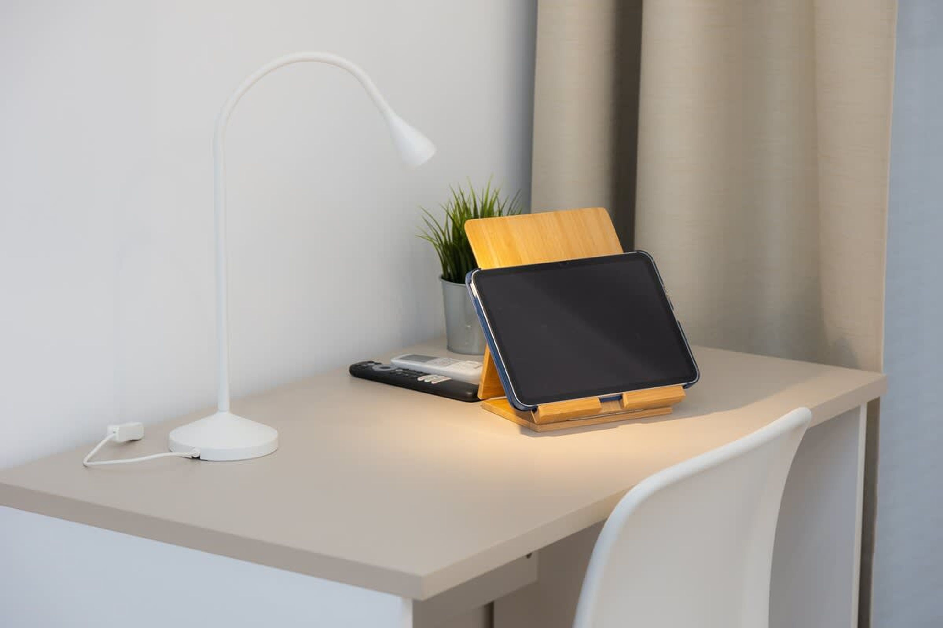 A desk with a tablet stand, a white desk lamp, a plant, and a remote control.
