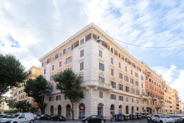 A multi-story building with a classical architectural style, featuring a corner entrance with arched doorways and a balcony on the second floor.