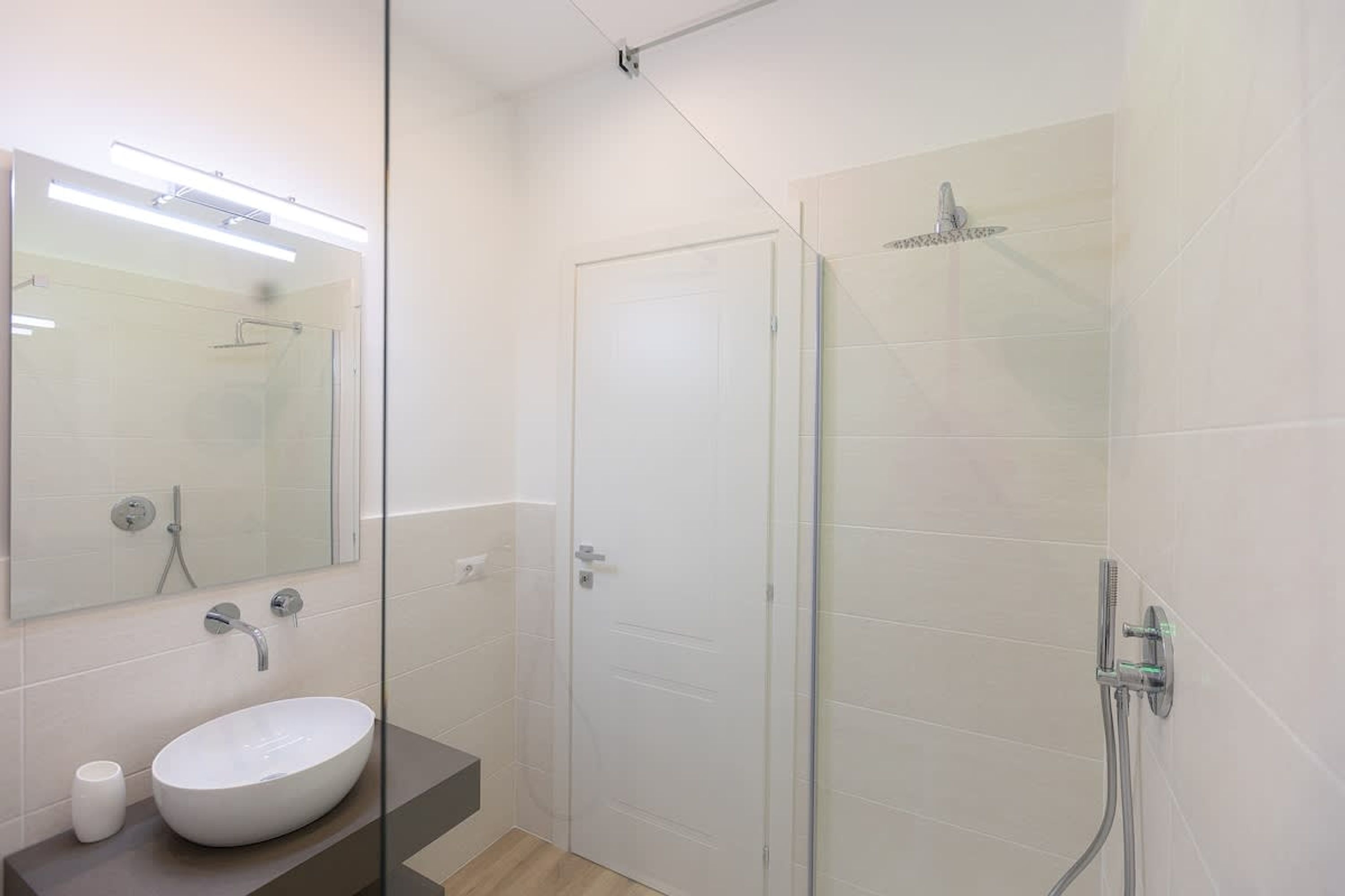 Un baño moderno con cabina de ducha de vidrio, un lavamanos blanco y un espejo sobre el lavamanos.