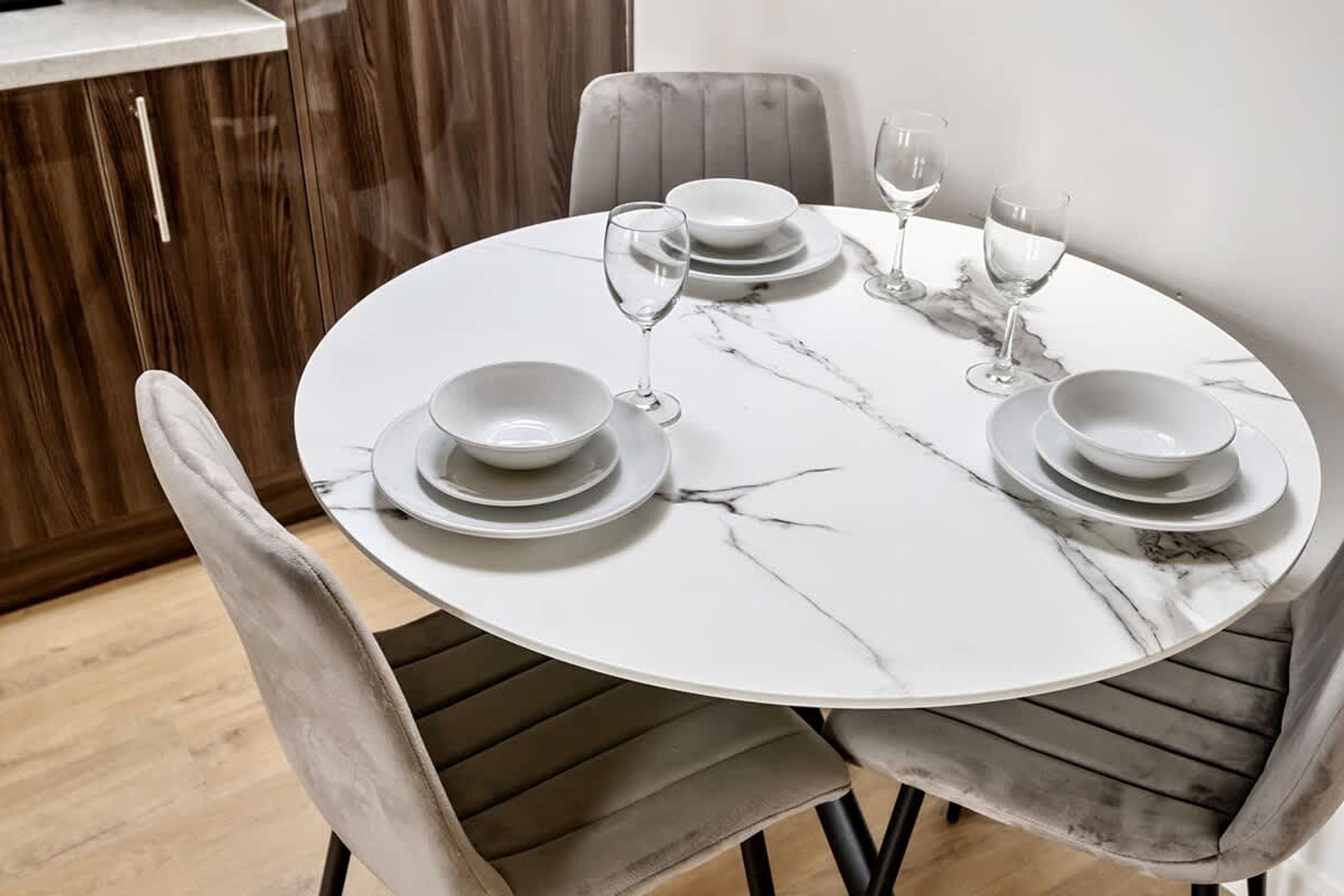 A round dining table with white marble top and grey upholstered chairs.
