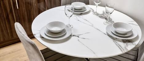 A round dining table with white marble top and grey upholstered chairs.
