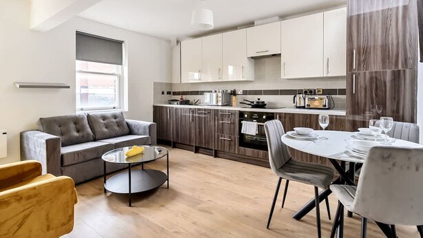 Een moderne keuken met donkerhouten kastjes, een inbouwoven en een eetgedeelte met een ronde tafel en stoelen.