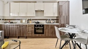 Een moderne keuken met houten kastjes, een inbouwoven en een eethoek met een ronde tafel en stoelen.