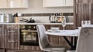 Een moderne keuken met een ingebouwde oven, een eettafel met stoelen en een aanrecht met een broodrooster en waterkoker.
