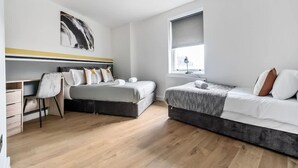 Een moderne slaapkamer met twee bedden, een bureau en een groot raam.