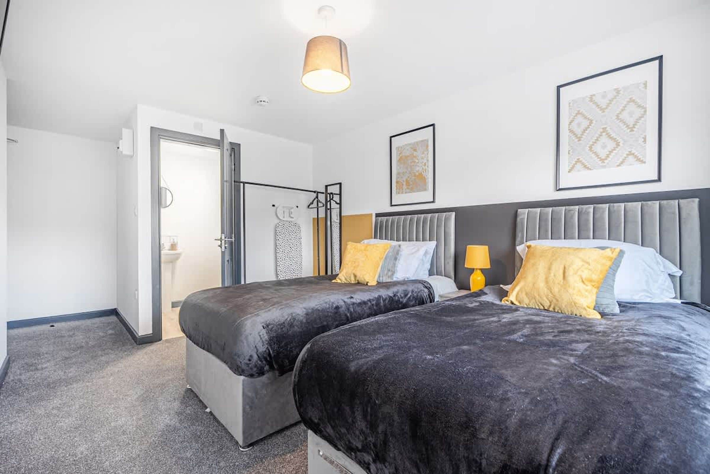 A hotel room with two beds, a wardrobe, a bathroom, and a ceiling light.