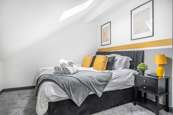 Une chambre à coucher moderne avec un lit, une table de chevet, une lampe et deux tableaux encadrés accrochés au mur.