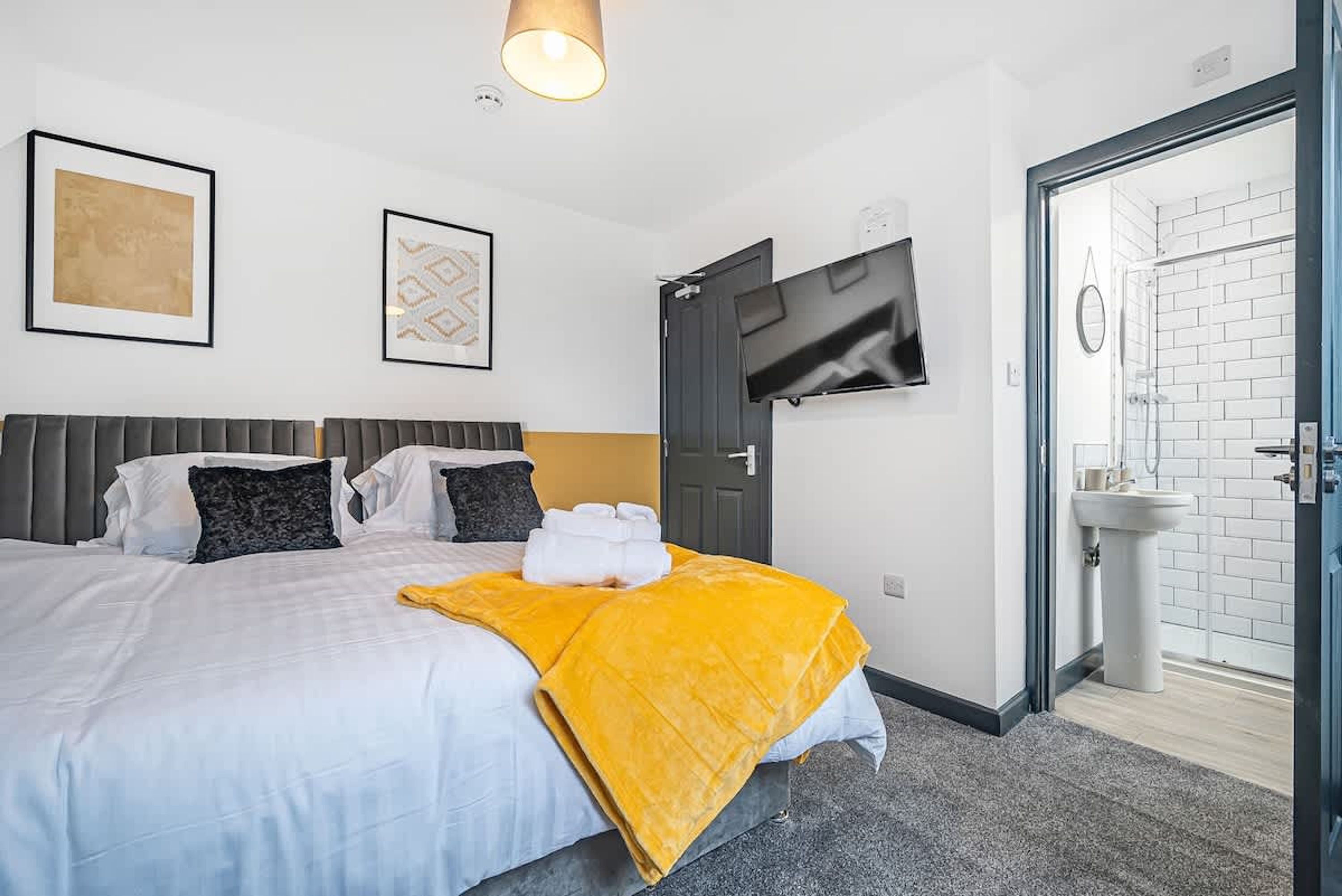 A hotel room with a bed, a TV mounted on the wall, a door leading to a bathroom, and a framed picture on the wall.