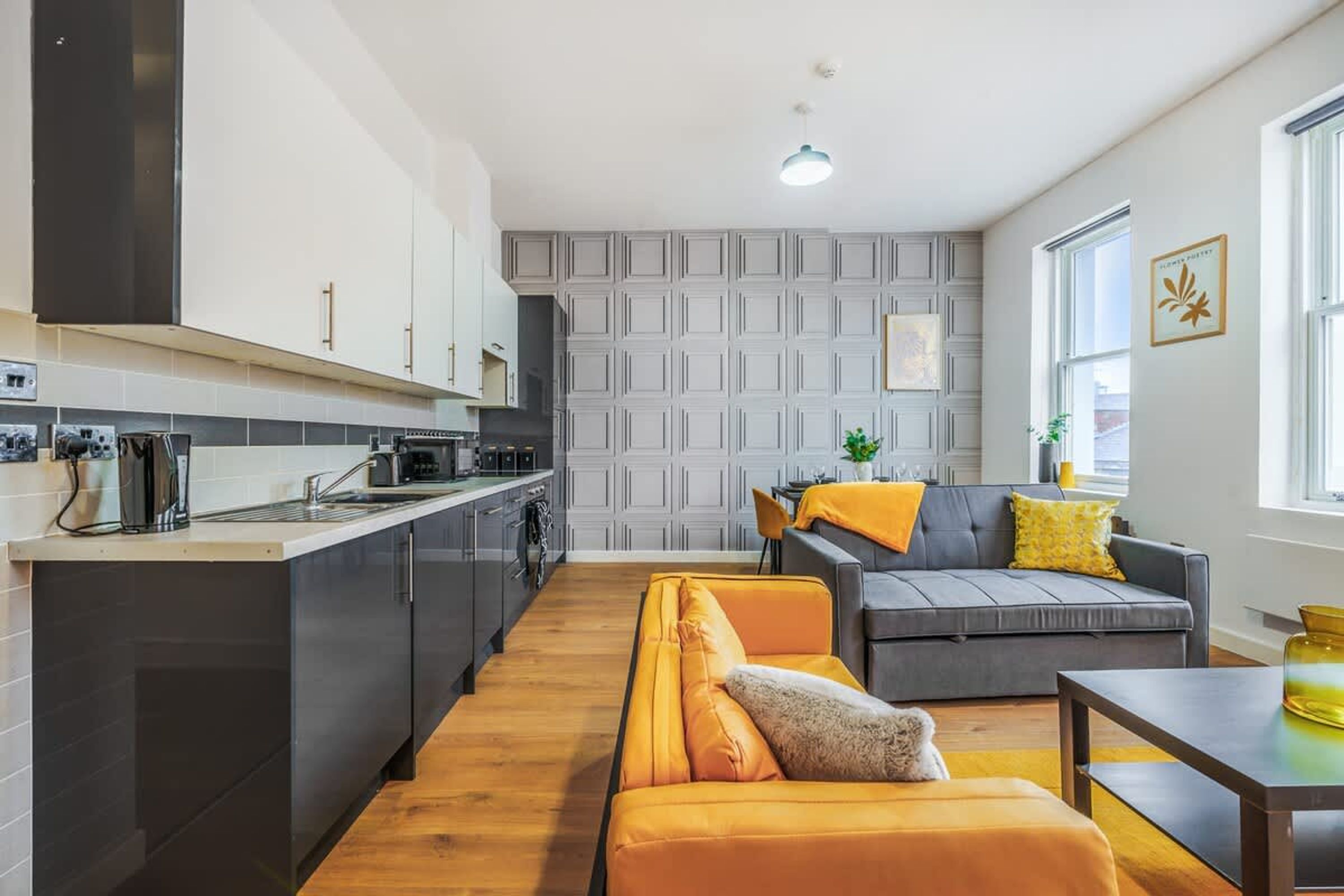 Una cocina moderna con armarios oscuros, un sofá gris con cojines amarillos y suelo de madera.