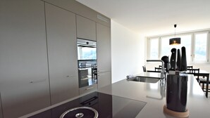 A modern kitchen with a central island, stainless steel appliances, and a view of the outdoors through large windows. - Dream View Apt With Homecinema Netflix Loggia (Kriens)
