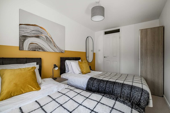 Une chambre avec deux lits, une grande peinture abstraite, un miroir et une armoire.
