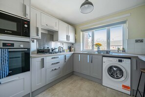 Eine moderne Küche mit weißen Schränken, einem Bosch-Backofen, einer Mikrowelle, einer Waschmaschine und einem großen Fenster mit Blick auf die Stadt.