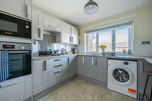 Una cocina moderna con armarios blancos, un horno Bosch, un microondas, una lavadora y un amplio ventanal con vistas a la ciudad.