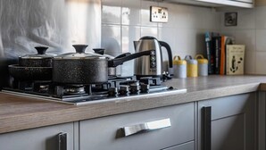 Una cocina con estufa a gas, ollas, tetera y cafetera.