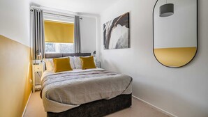 Un dormitorio moderno con cama, mesitas de noche, una ventana con cortinas, un espejo en la pared y un cuadro.