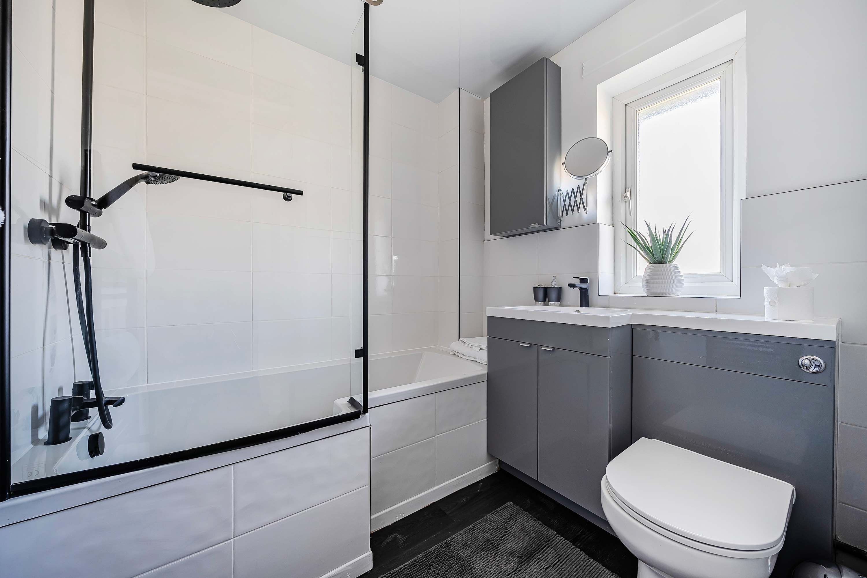 A modern bathroom with a glass-enclosed shower, a white bathtub, and a toilet.