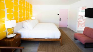 Une chambre d’hôtel moderne avec un lit, une table de chevet, une lampe et une porte rose.