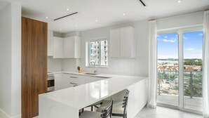Una cocina moderna con una isla grande, armarios blancos y vistas de la ciudad a través de amplios ventanales.