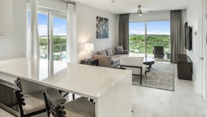 Habitación de hotel moderna con amplio comedor, sofá, televisor de pantalla plana y vista al exterior.