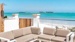 Un balcón con dos sofás color beige, un portón de madera y vistas a la playa y al océano.