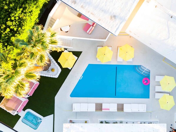 Ett poolområde på taket med en blå pool, vita solstolar, gula parasoller och en liten bubbelpool.