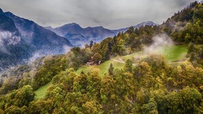 A mountainous landscape with a house surrounded by dense forest and rolling hills.