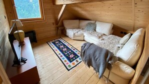 A cozy cabin with a wooden interior, a sofa, a small table with a lamp, and a window overlooking greenery. - Heidi Chalet - Panoramic View - Modern Part (Rossiniere)