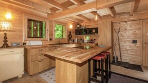 A wooden interior with a kitchen island, bar stools, and a wooden door. - Heidi Chalet - Panoramic View - Modern Part (Rossiniere)