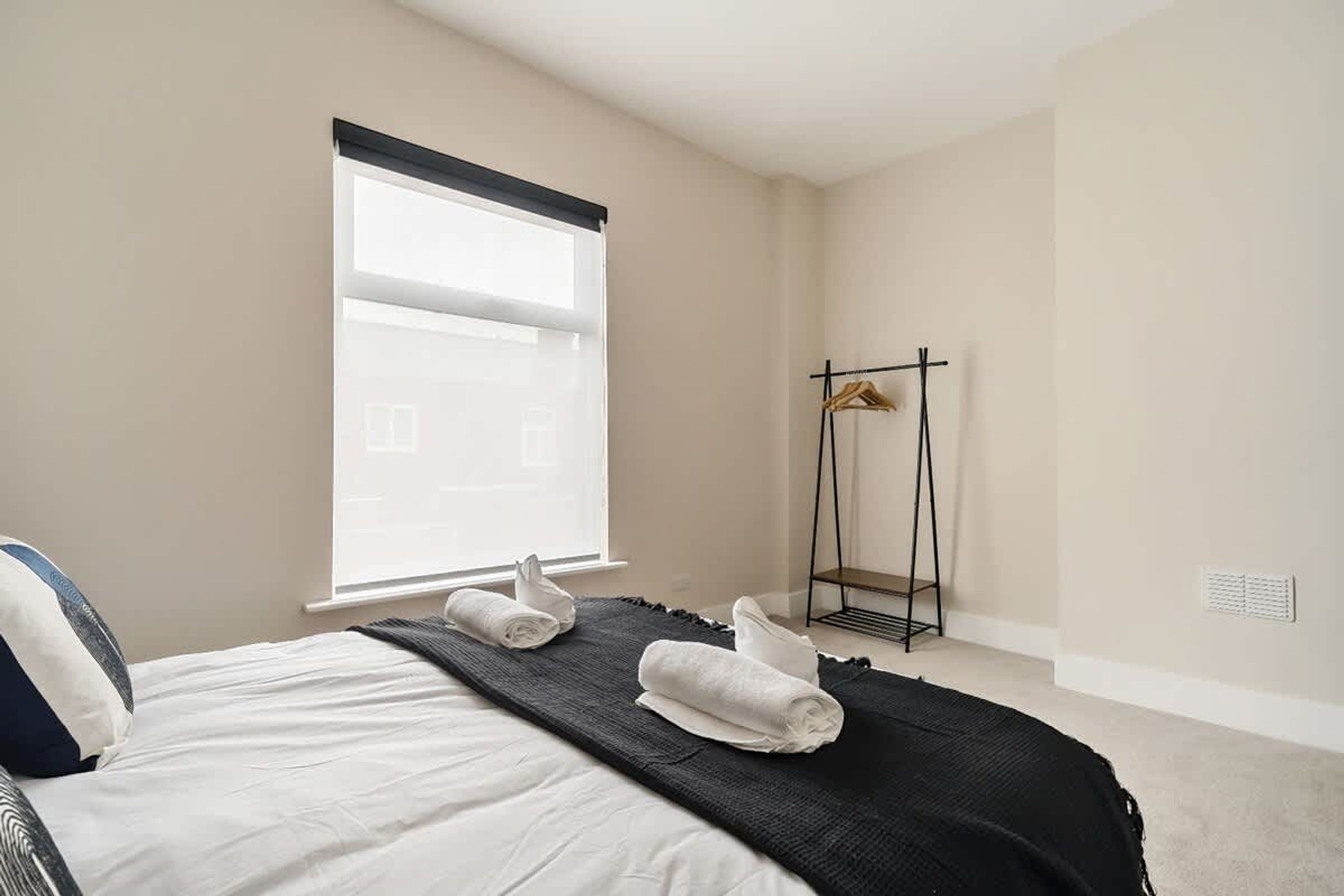 Camera d'albergo con un letto, una finestra con tende, un portasciugamani nero e una coperta decorativa nera.