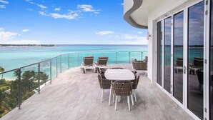 A balcony with a table and chairs, overlooking a turquoise sea and a clear sky. - Oceanfront Penthouse and Patio at ONE Cable Beach (Nassau)