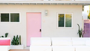 Zona de piscina amb un sofà exterior blanc, una porta rosa i una piscina amb vora de rajola.