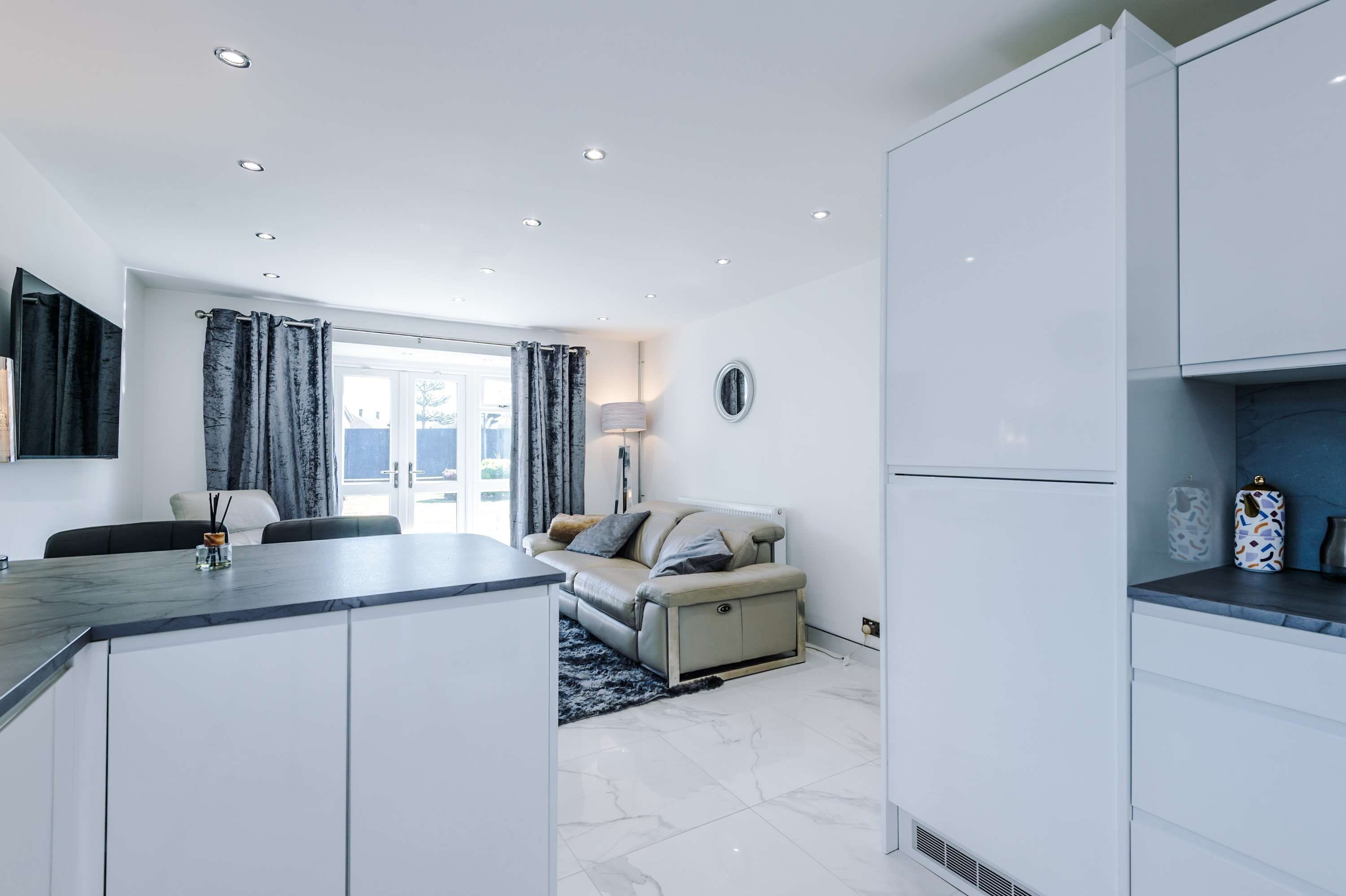 Eine moderne Küche mit weißen Schränken, ein Essbereich mit Tisch und Stühlen sowie eine Sitzecke mit Sofa.