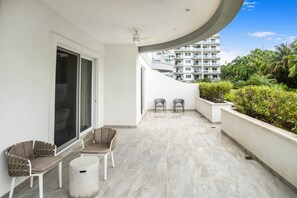 A balcony with a curved ceiling, two chairs, a small table, and a trash bin.