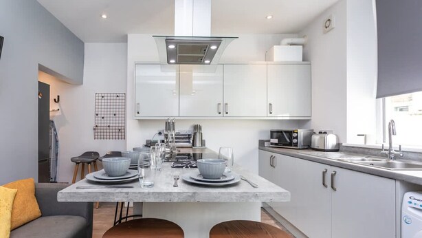 A modern kitchen with white cabinets, a central island with stools, and a built-in dishwasher. - Stylish Affordable Home in Burnley (Burnley)