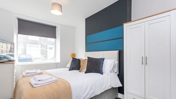 A bedroom with a bed, a window, a wardrobe, and a wall with a blue and black design. - Stylish Affordable Home in Burnley (Burnley)