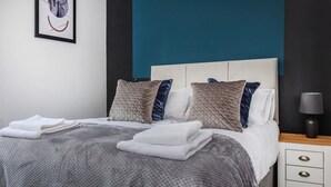 A neatly made bed with a grey blanket and pillows, a bedside table with a lamp, and a framed picture on the wall. - Stylish Affordable Home in Burnley (Burnley)