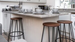 A modern kitchen with white cabinets, a stainless steel range hood, a built-in microwave, and a large island with stools. - Stylish Affordable Home in Burnley (Burnley)