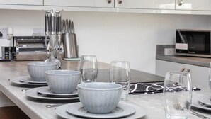 A modern kitchen with a marble countertop, white appliances, and neatly arranged dining ware. - Stylish Affordable Home in Burnley (Burnley)