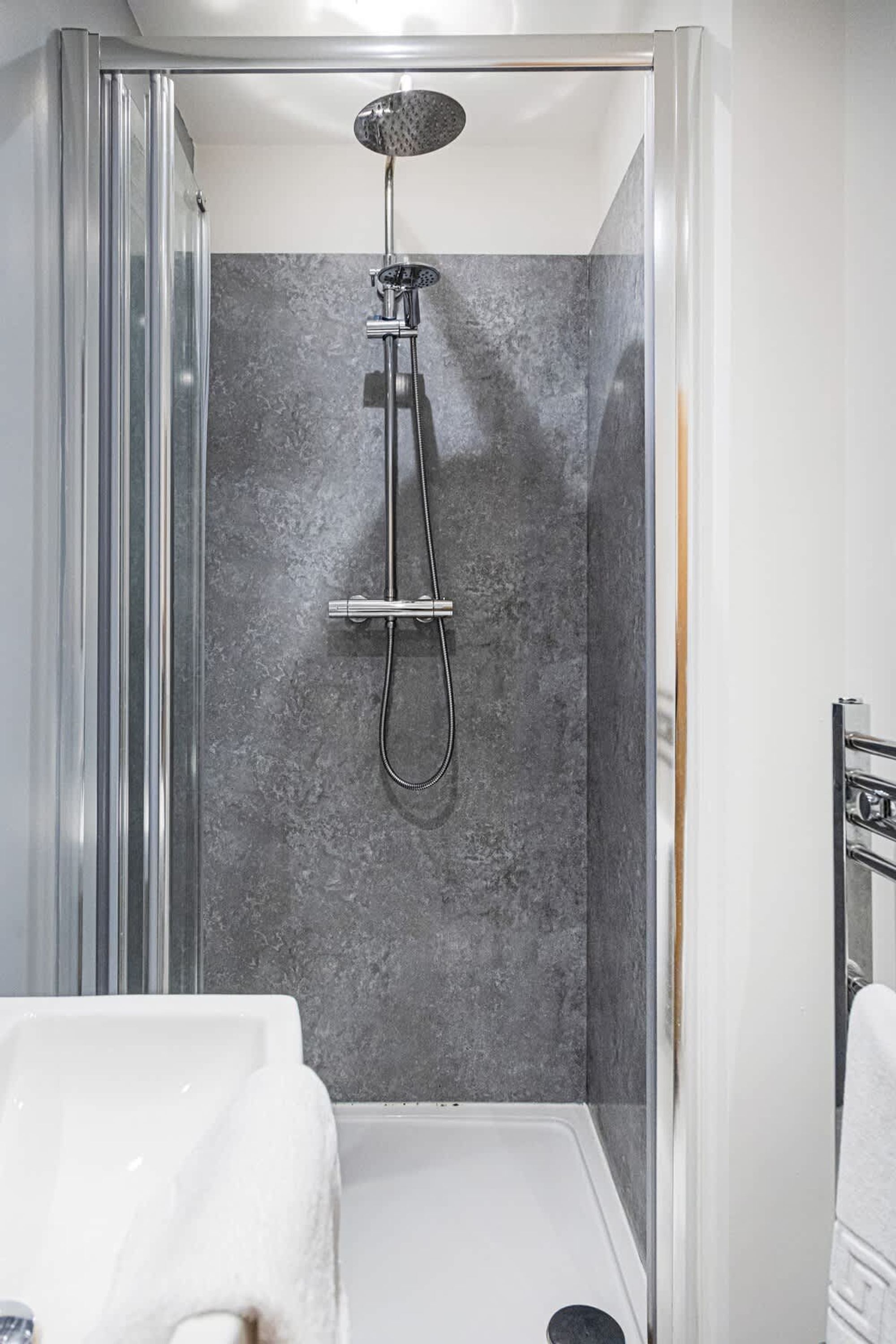 A modern shower enclosure with a glass door, a handheld showerhead, and a wall-mounted control panel.