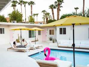 A pool area with lounge chairs, yellow umbrellas, and a pink flamingo float. - Deluxe Room, 1 King Bed, Kitchen, Pool View (Palm Springs)