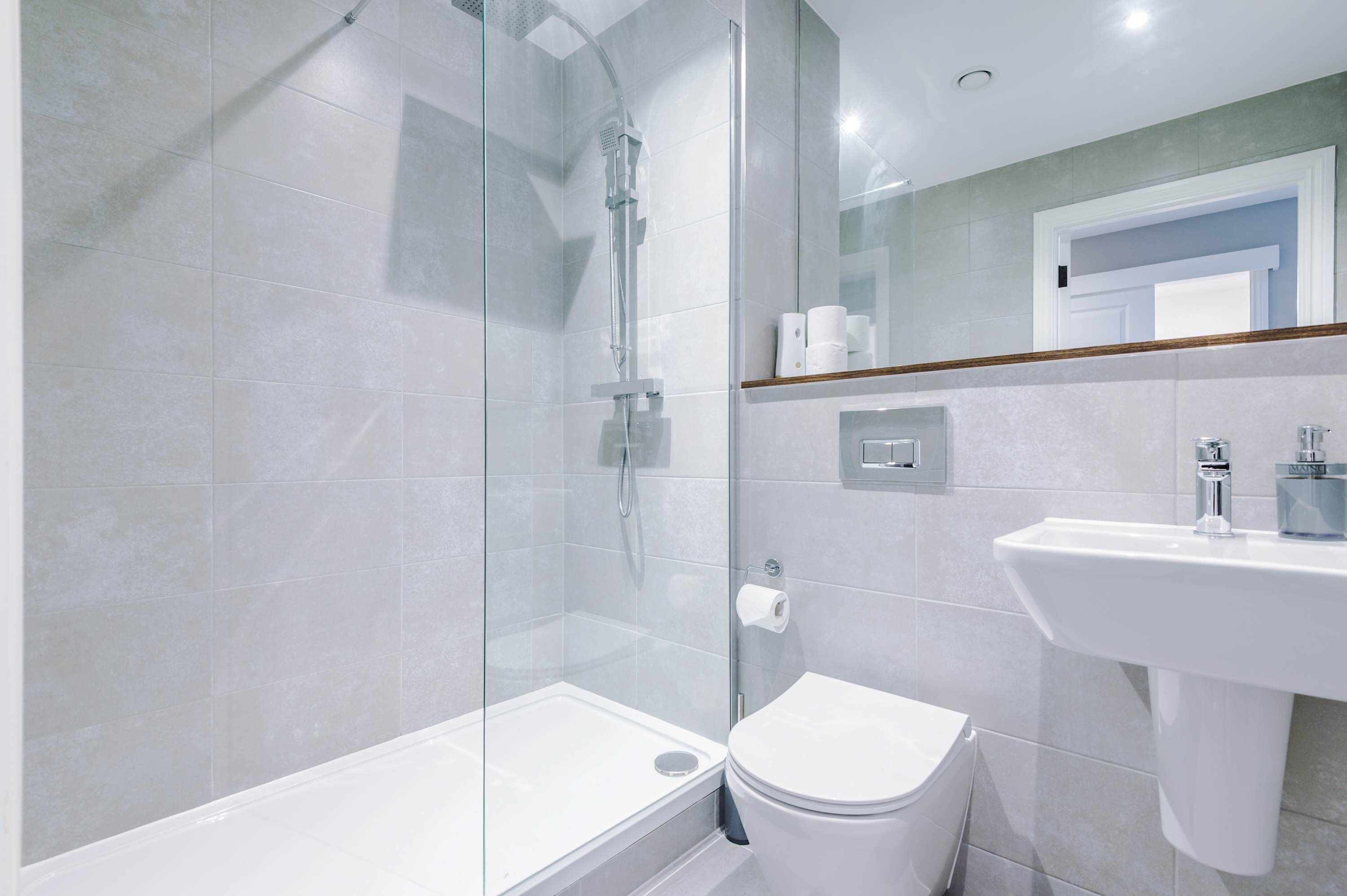 Une salle de bain moderne avec une douche à parois de verre, des toilettes blanches et un lavabo avec un miroir au-dessus.