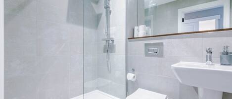Une salle de bain moderne avec une douche à parois de verre, des toilettes blanches et un lavabo avec un miroir au-dessus.