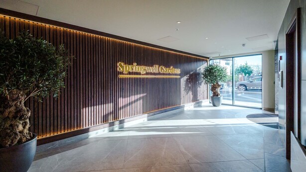 A reception area with a wooden panel wall, a large potted plant, and a sign reading "Springwell Gardens." - Stylish City Centre Apartment (Leeds)
