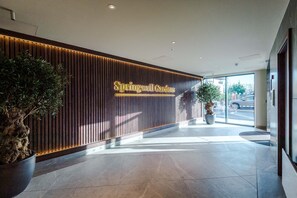A reception area with a wooden panel wall, a large potted plant, and a sign reading "Springwell Gardens." - Stylish City Centre Apartment (Leeds)