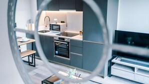 A modern kitchen with a microwave, oven, and sink, a dining area with a table and chairs, and a TV in the living room. - Stylish City Centre Apartment (Leeds)