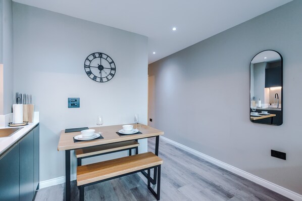 A modern dining area with a wooden table, bench, and a wall clock. - Stylish City Centre Apartment (Leeds)