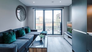 A modern living room with a grey sofa, a coffee table, and a large window. - Stylish City Centre Apartment (Leeds)